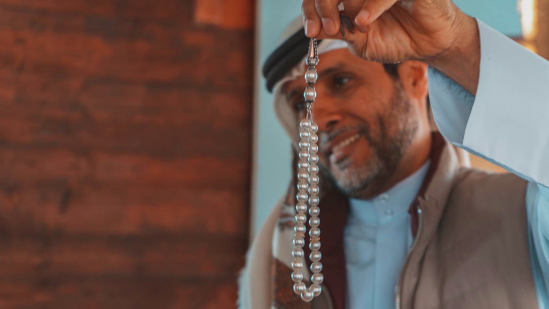 Man holding up a pearl necklace strand against brick wall background